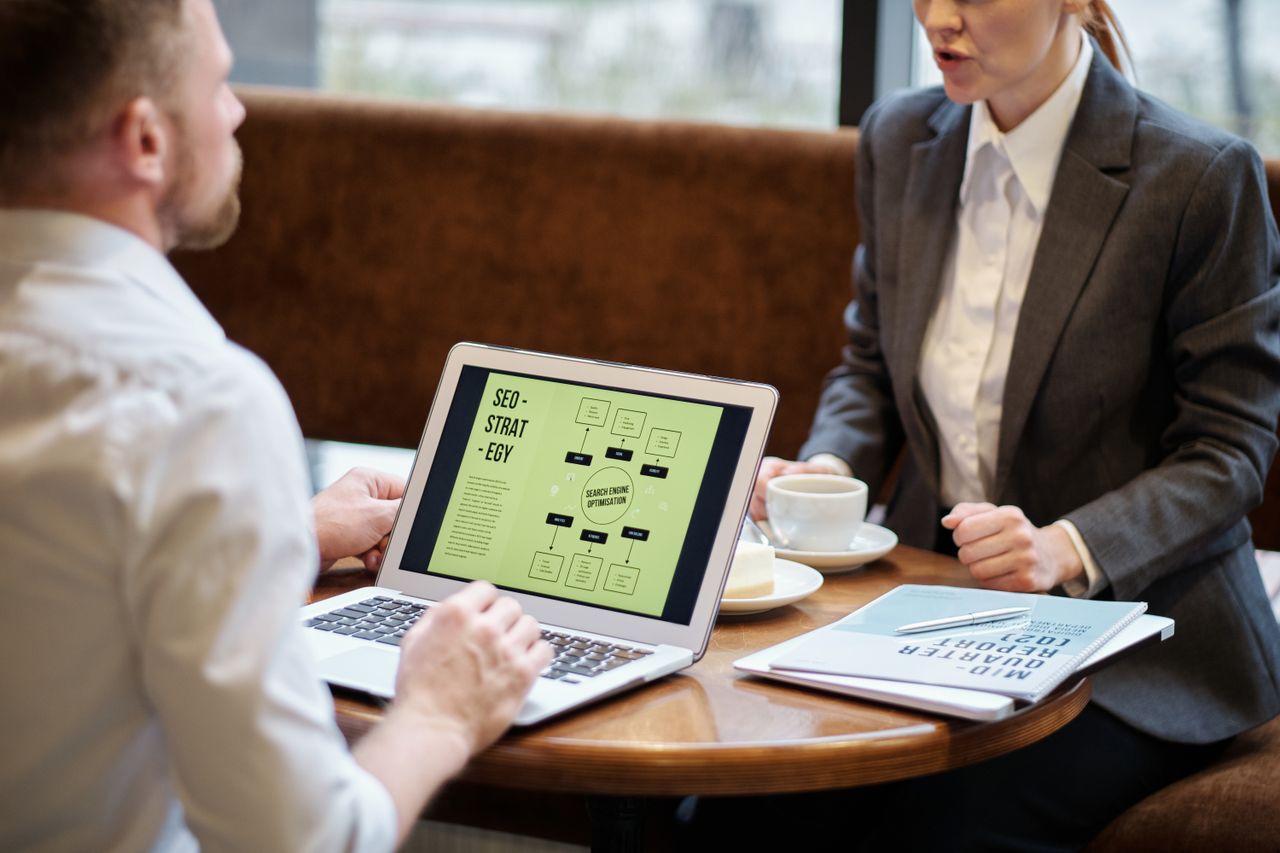 The Art of Drawing Readers In: Your attractive post title goes here A man and woman engaged in a business meeting discussing SEO strategy in a cozy cafe setting.